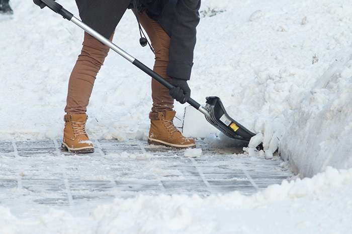 Business woman with shovel cleaning snow filled street in front of the office at work