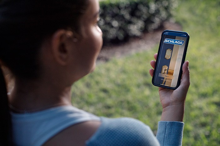 Young woman using her smart phone to lock her front door remotely.