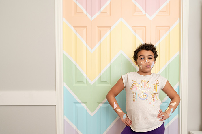 Child posing in front of bifold doors that have painted with stripes.